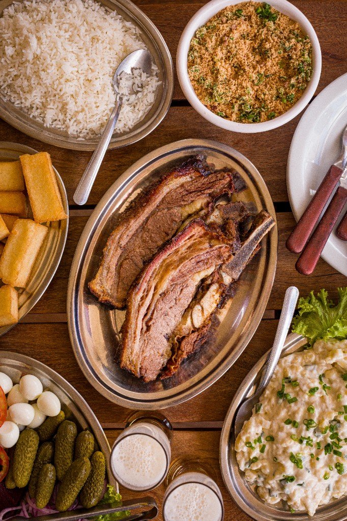 Mesa com costela, arroz, farofa, mandioca e salada